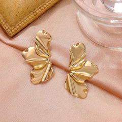 A pair of gold-toned, irregular petal-shaped stud earrings resting on a soft fabric surface.