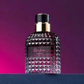 A glass perfume bottle with a textured, studded surface and a gold cap sits on a blue surface.