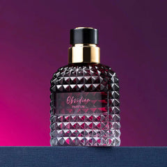 A glass perfume bottle with a textured, studded surface and a gold cap sits on a blue surface.