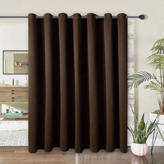 A single dark brown blackout curtain with silver grommets hangs on a rod as a room divider.
