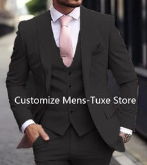 A man wears a slim-fit black three-piece suit with a white dress shirt and a pink necktie.