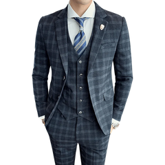 A man wearing a slim-fit, dark grey plaid three-piece suit with a white shirt and blue tie.