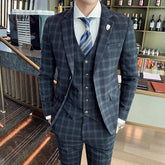 A man wears a slim-fit, dark grey plaid three-piece suit with a white shirt and blue tie.