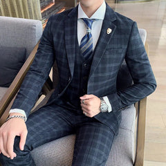 A man wears a dark grey plaid three-piece suit with a white shirt and a blue patterned tie.