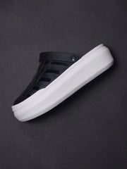 A black closed-toe platform sandal with a thick white sole on a dark background.