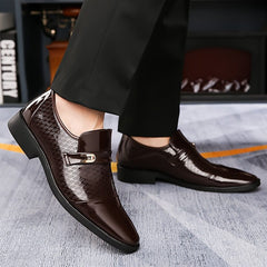 A pair of dark brown faux patent leather slip-on dress shoes with a textured finish and metal buckle.