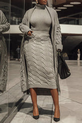 A woman wears a long, ash-gray cable knit cardigan over a matching turtleneck and midi skirt.