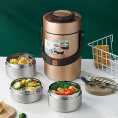 A gold vacuum insulated lunch box with three stainless steel food containers on a table.