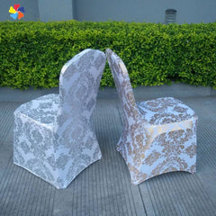 Two white spandex banquet chair covers featuring a metallic gold damask print pattern.