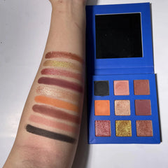 A nine-color eyeshadow palette with shimmer and matte shades shown swatched on an arm.