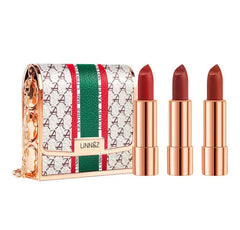 A set of three lipsticks with rose gold tubes displayed next to a patterned handbag.