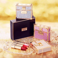 Three glittery, box-shaped bags with gold chains are displayed alongside three lipsticks.