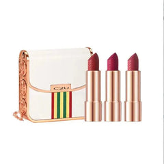 A white handbag-shaped case with a gold chain and three matte lipsticks in rose gold tubes.
