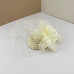 A cream-colored bridal fascinator featuring a mesh veil, fabric flower, and delicate feathers.