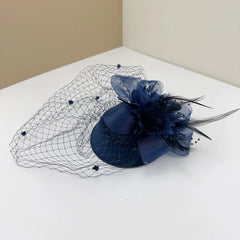 A navy blue retro bridal fascinator featuring a mesh veil, fabric flower, and feather accents.