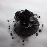 A black fascinator hair clip featuring a satin rose and a dotted mesh veil.