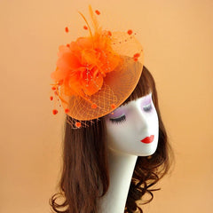 A bright orange fascinator hat featuring a large flower, feathers, and netting on a mannequin head.