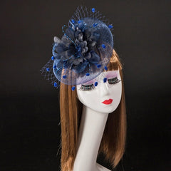 A blue fascinator headpiece featuring a large fabric flower and netting on a mannequin head.