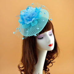 A light blue fascinator hat featuring a floral accent, feathers, and a decorative mesh veil.