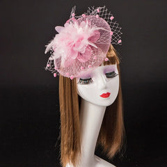 A pink fascinator headpiece featuring a floral accent, feathers, and a dotted mesh veil.