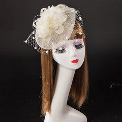 A cream-colored fascinator headpiece with a flower, netting, and pearl accents on a mannequin head.