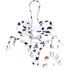 A white bikini set with a black cow print pattern, featuring a hollow-out top and tie-side bottoms.