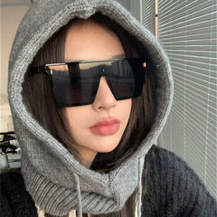 A person wears oversized, rectangular, one-piece black sunglasses with a grey knit hood.