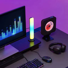 A vertical RGB light bar stands on a desk next to a computer monitor and a music player.