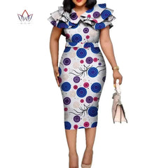 A woman wears a knee-length, white cotton dress with a colorful circular print, ruffled collar, and belt.
