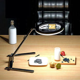 A black ring light with an integrated phone holder mounted on a foldable tripod stand.