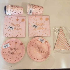 A rose gold birthday party tableware set including paper plates, cups, napkins, and a banner.