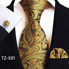 A gold and black paisley patterned necktie, pocket square, and cufflink set worn with a suit.