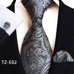 A black and silver paisley patterned necktie, pocket square, and matching cufflink set.