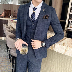 A man wears a navy blue plaid three-piece suit consisting of a blazer, vest, and matching pants.
