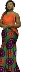 A woman wears a long, one-shoulder dress featuring an orange bodice and a green patterned skirt.
