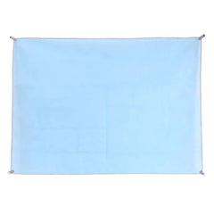 A rectangular light blue sand-free beach mat with corner loops for securing it to the ground.