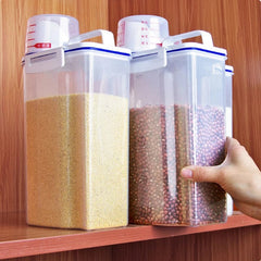 Two transparent plastic food storage containers with white lids and measuring cups on a shelf.