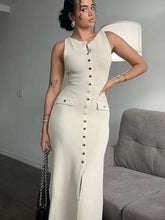 A woman wears a sleeveless, apricot-colored ribbed maxi dress with a button-down front and slit.