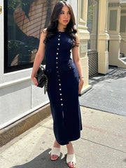 A woman wears a sleeveless navy blue midi dress with a button-down front and a high leg slit.