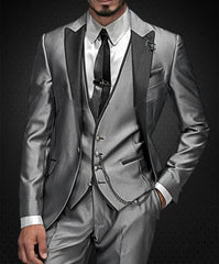 A man wears a shiny grey three-piece suit with a black lapel, vest, and pocket chain.