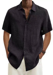 A man wears a loose-fitting, short-sleeved black cotton linen shirt with a point collar.