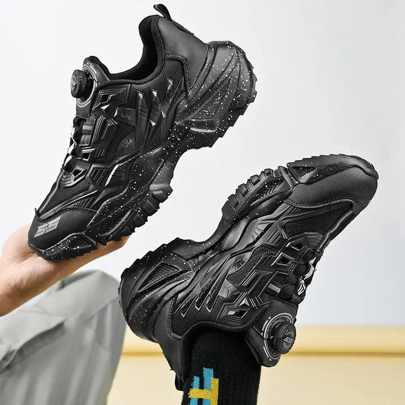 A pair of men's luxury sneakers with thick, textured soles and white speckles. These black lace-free trainers feature a dial-style closure and are worn with black socks; perfect for casual or running use.