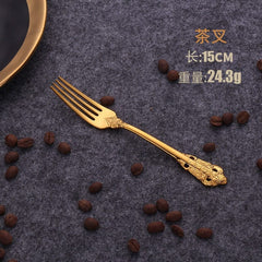 A golden stainless steel dessert fork with ornate relief detailing on the handle.
