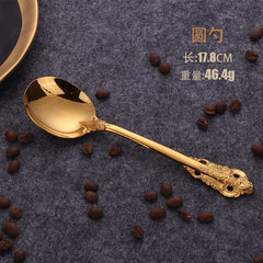 A gold-colored stainless steel spoon with an ornate relief pattern on the handle, measuring 17.8 centimeters in length.