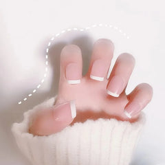 A hand wearing long, square-shaped French tip press-on nails with a natural pink base.