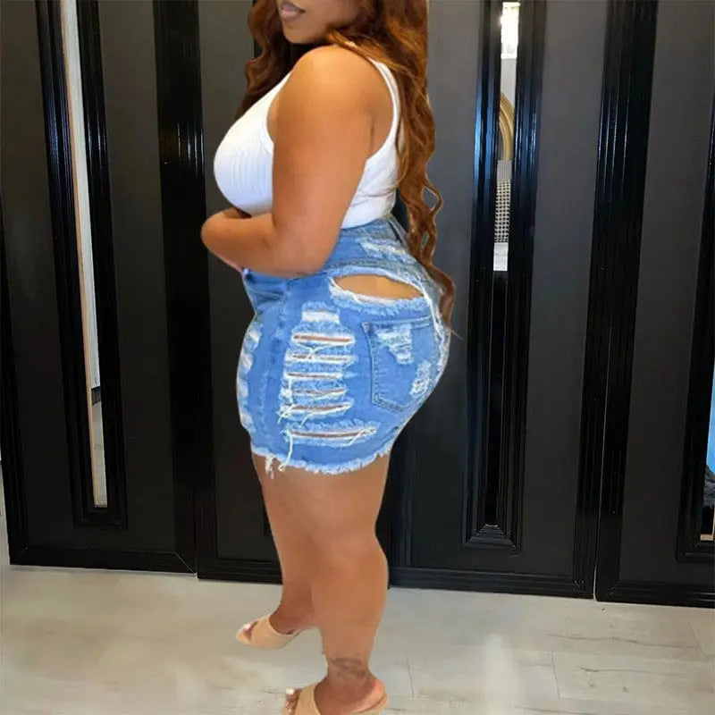 A woman wearing blue denim shorts with heavy distressing and a raw hem.