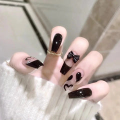 A hand displays mid-length coffin-shaped press-on nails featuring black polish and bow accents.