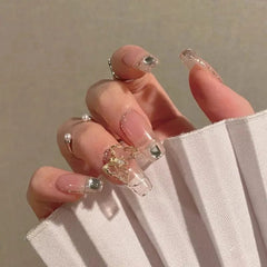 A hand displays mid-length coffin-shaped press-on nails with a clear finish and gold accents.