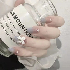 A hand holds a glass jar, showcasing mid-length coffin-shaped press-on nails with a blue ombre.