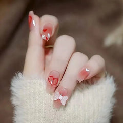 A set of mid-length coffin-shaped press-on nails featuring a pink gradient with heart and bow art.